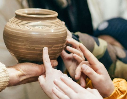 Barnhänder rör vid en drejad keramikskål och utforskar form och yta i en skapande miljö